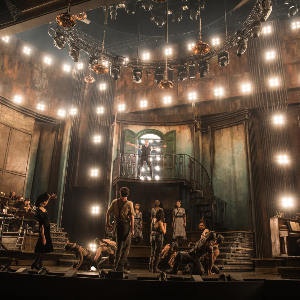 Hadestown live on stage - photo shows Hades atop a balcony with other performers below. A live band is also on stage